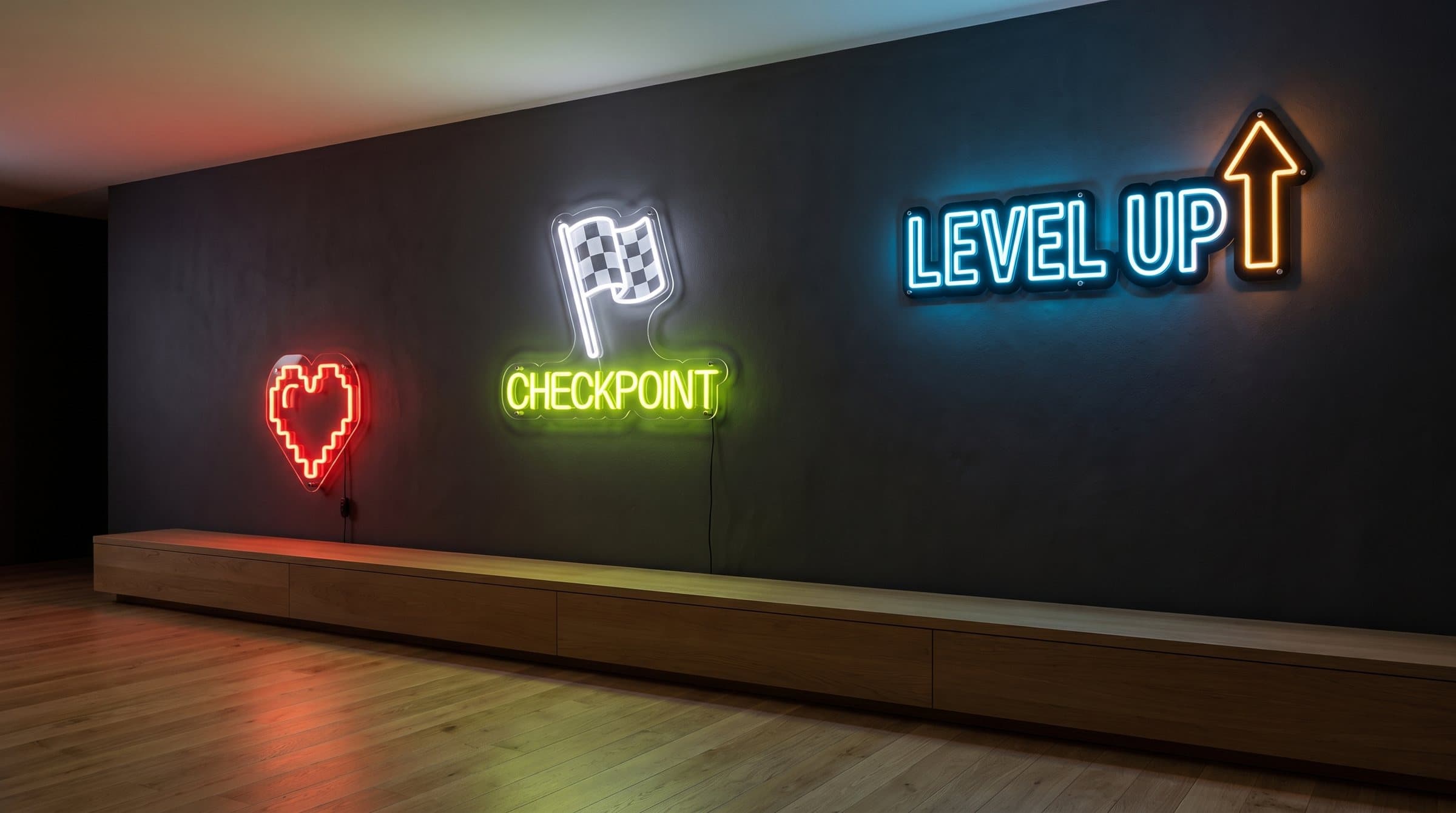 Un mur anthracite la nuit avec trois néons allumés : un cœur rouge, le drapeau Checkpoint vert lime et Level Up bleu et ambre